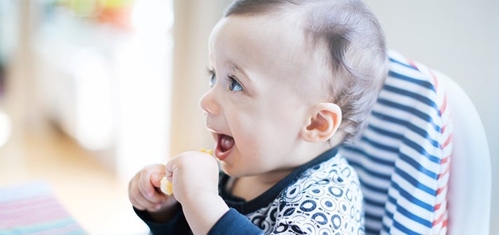 baby happily picking up food while in highchair