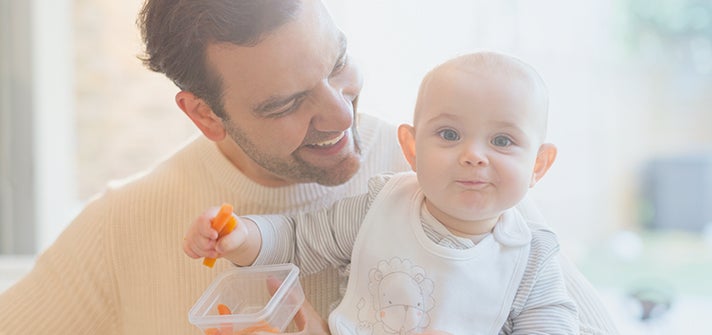 baby sitting on caregivers lap with carrot in their hand