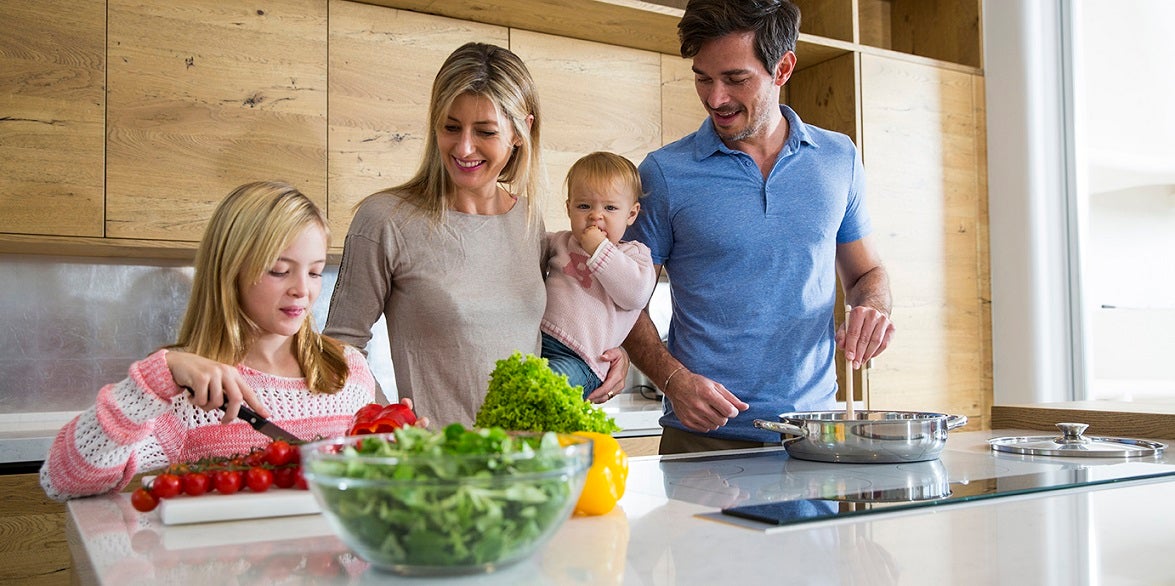 baby being held by mother while another child chops tomatoes