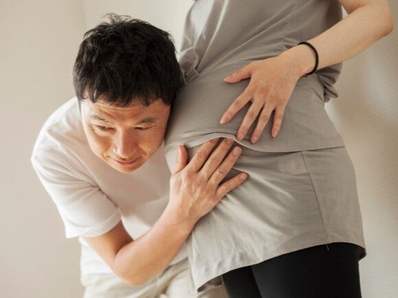 man with ear against pregnant woman's stomach man with ear against pregnant woman's stomach