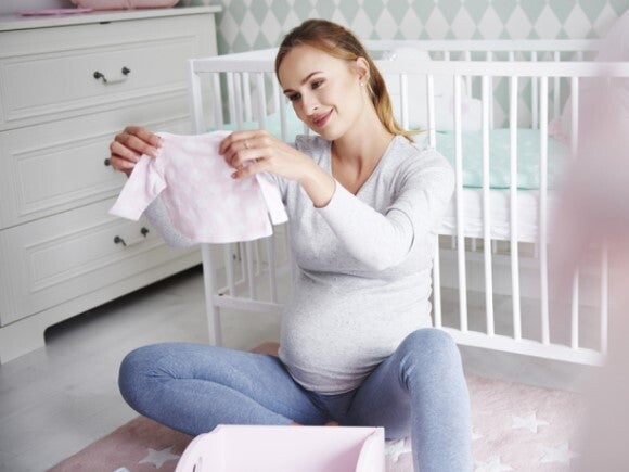 pregnant woman looking at newborn clothes pregnant woman looking at newborn clothes