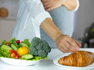 Pregnant woman with a salad and croissant in front of her Pregnant woman with a salad and croissant in front of her