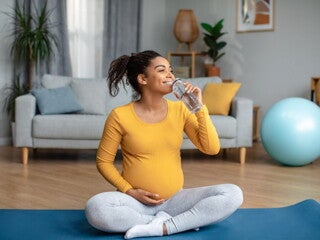 Pregnant woman sitting on a yoga mat drinking water Pregnant woman sitting on a yoga mat drinking water