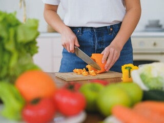 Woman chopping up capsicum on a chopping board with vegetables and fruits around Woman chopping up capsicum on a chopping board with vegetables and fruits around