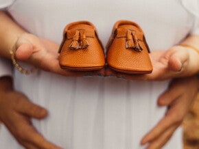 Pregnant woman holding a pair of brown baby shoes