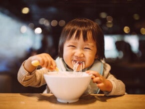 toddler eating noodles from a bowl at a restaurant toddler eating noodles from a bowl at a restaurant