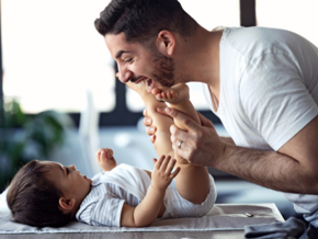Baby laying down and father making the baby laugh leaning over