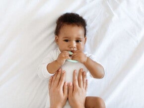 Baby lying down on bed with parents hands rubbing belly
