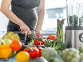 Pregnant woman in dark top cutting vegetables Pregnant woman in dark top cutting vegetables