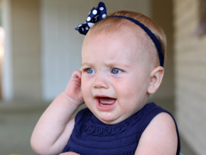 Baby in blue dress crying and pulling on ear Baby in blue dress crying and pulling on ear