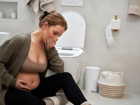 Pregnant lady sitting on the ground in a bathroom with her hand over her mouth Pregnant lady sitting on the ground in a bathroom with her hand over her mouth