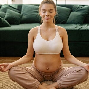 Pregnant woman meditating in a white crop and brown pants