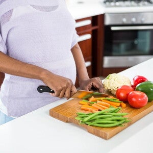 Pregnant woman wearing a purple top chopping vegetables