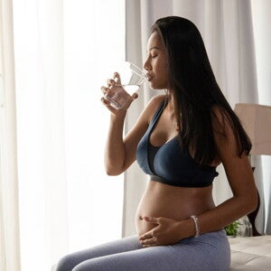 Pregnant woman drinking water whilst holding her belly