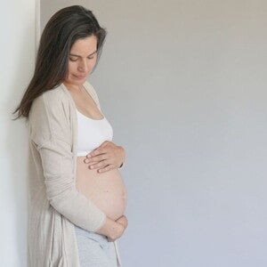 Pregnant woman in grey cardigan and white crop holding her belly