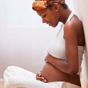 Pregnant woman in white pants and top holding her belly