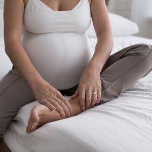 Pregnant woman in white shirt and grey pants sitting on a bed
