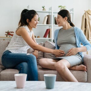 Pregnant woman and friend touching her belly