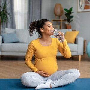 Pregnant woman sitting on a yoga mat drinking water