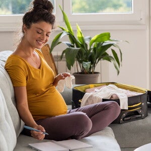 Pregnant woman packing her hospital bag using a list