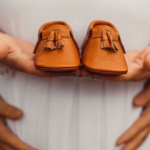 Pregnant woman holding a pair of brown baby shoes