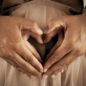 Couple holding hands in the shape of a heart over a pregnant belly