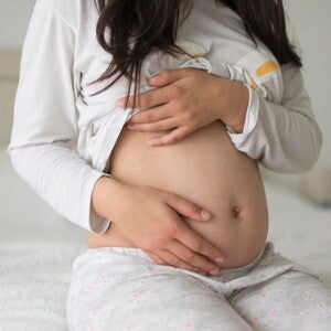 Pregnant woman wearing grey holding her belly