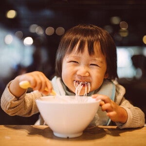 toddler eating noodles from a bowl at a restaurant