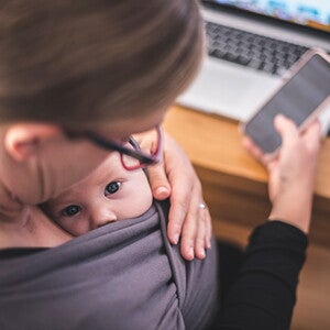 Woman on the phone with baby in grey carrier 