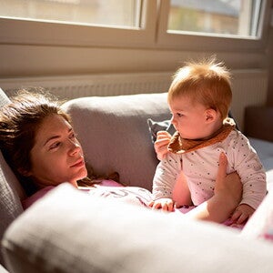 Woman lying on the couch in pyjamas with baby on her lap