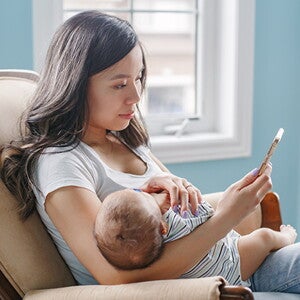 Woman sitting on couch holding her sleeping baby while on the phone