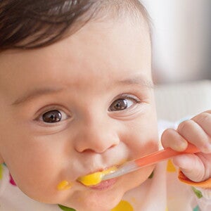 Infant grinning and eating puree.