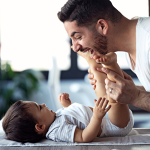 Baby laying down and father making the baby laugh leaning over