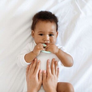 Baby lying down on bed with parents hands rubbing belly