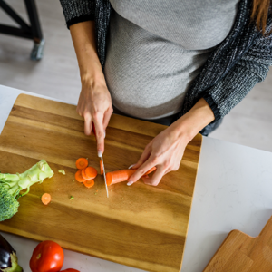 Pregnant woman cutting carrots on a wooden chopping board