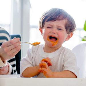 Mother feeding upset toddler boy with spoon