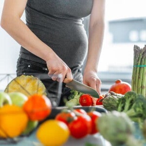 Pregnant woman in dark top cutting vegetables