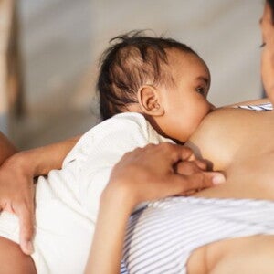 Mother in striped top breastfeeding her baby in a white onesie 