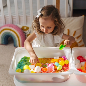 Toddler girl playing with colorful sand and toys