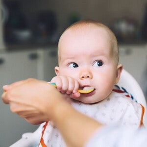 baby eating puree off a spoon in highchair with parents help