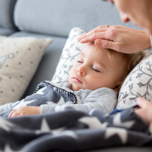 Toddler laying down with mothers hand on toddlers head