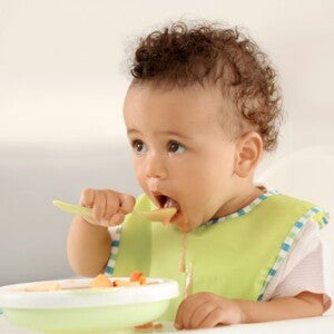 baby eating with bib on with a spoon and bowl