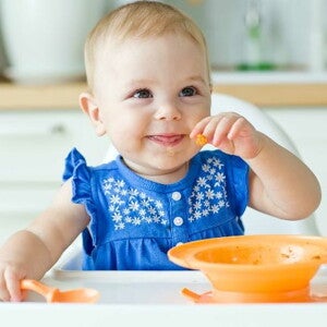 9 month old girl eating with spoon and bowl