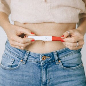 Woman holding a positive pregnancy stick over her stomach