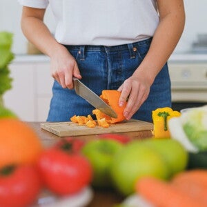 Woman chopping up capsicum on a chopping board with vegetables and fruits around