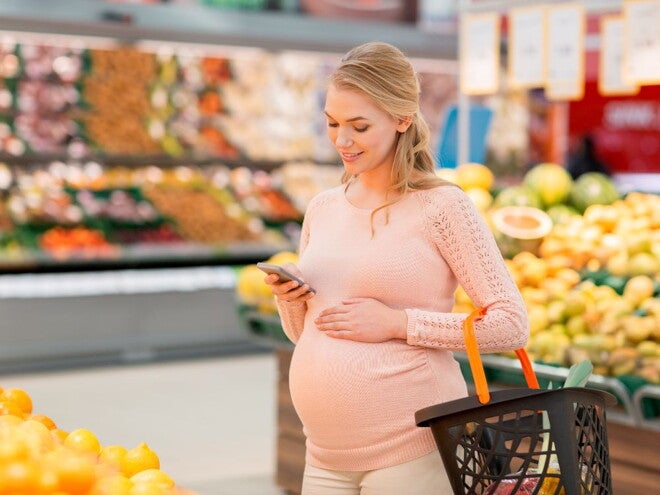Pregnant woman grocery shopping in the produce section Pregnant woman grocery shopping in the produce section