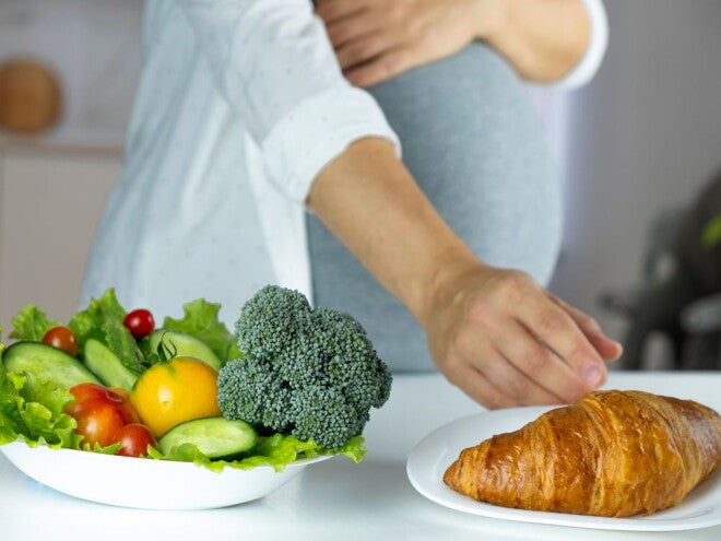 Pregnant woman with a salad and croissant in front of her Pregnant woman with a salad and croissant in front of her
