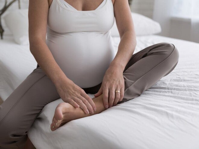 Pregnant woman in white shirt and grey pants sitting on a bed Pregnant woman in white shirt and grey pants sitting on a bed