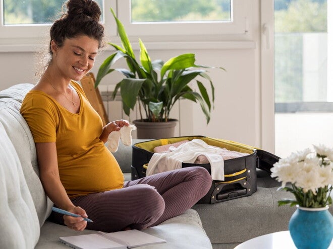 Pregnant woman packing her hospital bag using a list Pregnant woman packing her hospital bag using a list