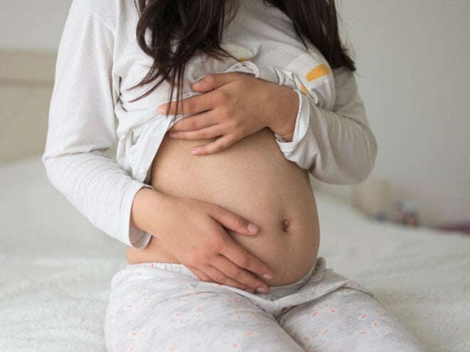 Pregnant woman wearing grey holding her belly Pregnant woman wearing grey holding her belly